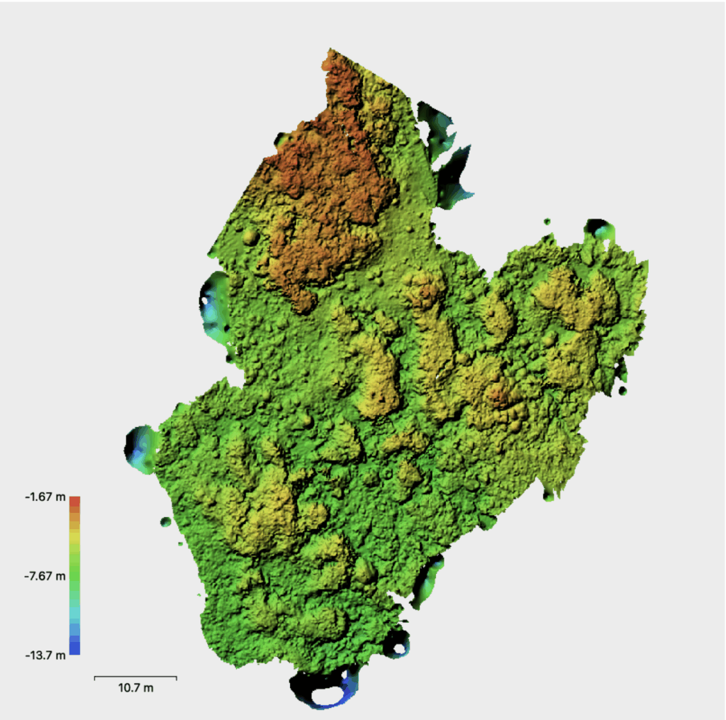 3D bathymetric map of a coral reef structure, colored by elevation, showing higher areas in red and lower areas in blue with depth scale and meter reference bar.